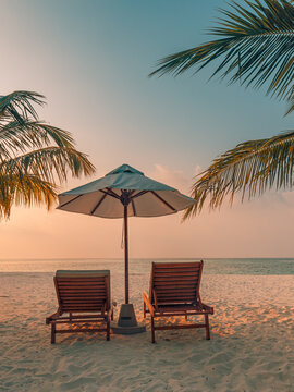 Romantic sunset sky tropical beach two sunbeds umbrella palm trees calm sea sandy shore evening summer paradise. Perfect summer vacation travel scene. Luxury honeymoon couples relax sunset getaway