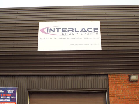 Ottawa, Ontario, Canada &ndash; July 17, 2026: : A white sign reading "INTERLACE GROUP EVENTS AUDIO VISUAL . ENTERTAINMENT . PRODUCTION . STAGING . SALES" mounted on a dark ribbed industrial wall on Canotek