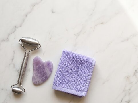 Facial roller and gua sha with towel on marble surface