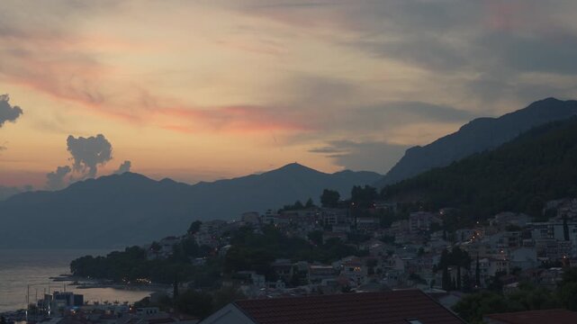 Day to night transition time lapse over Baska Voda resort town on a hillside in Croatia. City lights turn on as dusk turns into dark night. Scenic coastal evening during summer vacation.