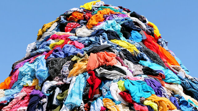 Enormous Heap Of Colorful Discarded Clothing Material Piled Outdoors Under Clear Sky   