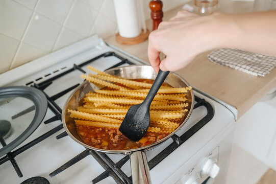 Cooking Italian pasta boiling in a stainless steel pot on a modern kitchen stove, home culinary preparation concept
