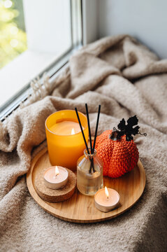 Cozy autumn still life with a burning candle, mini decorative pumpkin and warm knitted throw blanket, seasonal mood