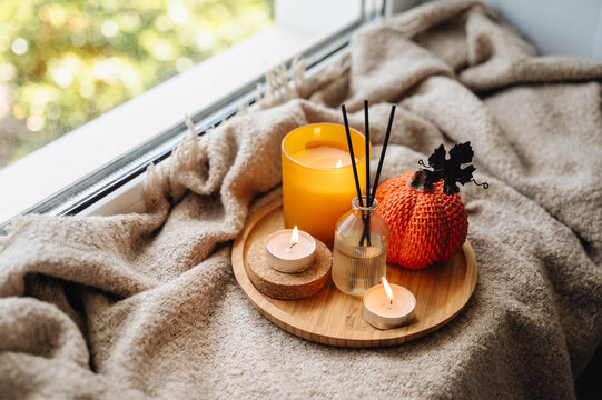 Cozy autumn still life with a burning candle, mini decorative pumpkin and warm knitted throw blanket, seasonal mood