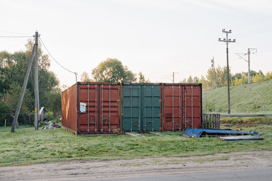 Red and green cargo shipping containers placed on grass near utility poles and power lines, industrial storage concept