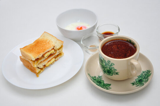 Kopitiam breakfast set, kopi susu (torrefacto coffee with condense milk), soft boiled egg served with pepper and soy sauce, and kaya toast, served at a white top table