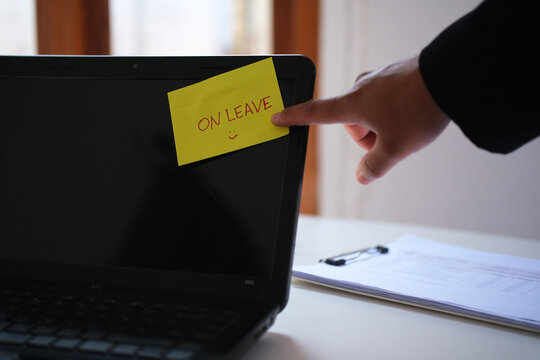 An employee's hand is pointing at a notice reading "On Leave" on a laptop screen&mdash;taking time off, a break from work, or a vacation.