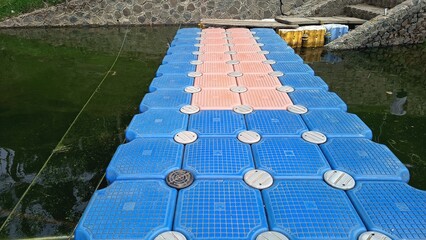 Floating modular pontoon dock made of blue and orange plastic cubes on a calm lake © Untung