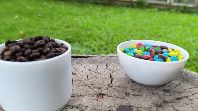 A white cup with coffee beans in a summer garden, with colorful candies nearby.