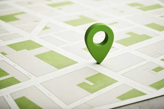Green three-dimensional location marker standing upright on a printed street map showing abstract urban grid layout with beige and olive colored blocks and intersecting roads under bright even