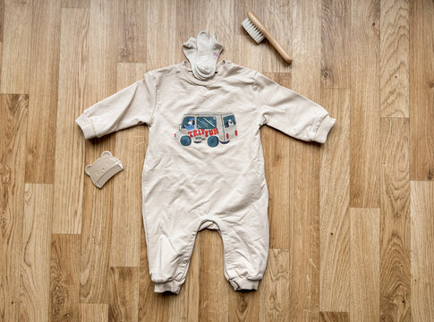 Top view composition of newborn organic cotton romper with vehicle print, socks, wooden baby hairbrush and silicone teether on wooden background. Ideal for nursery content.