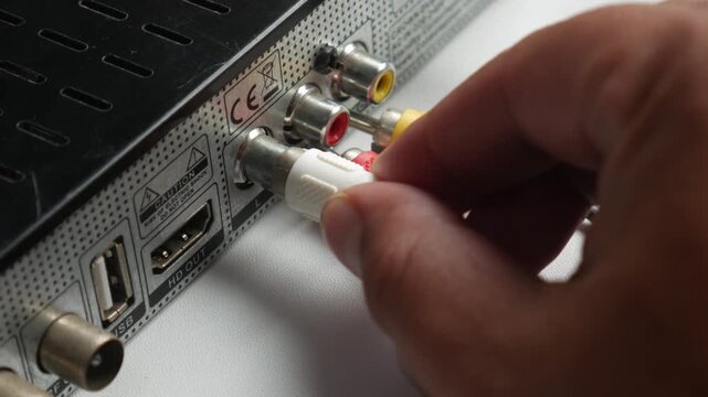 A man's hand is connecting an audio jack to a device against a white background.
