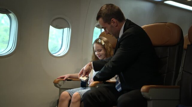 Businessman traveling with his daughter inside a commercial airplane cabin, representing family travel and business mobility