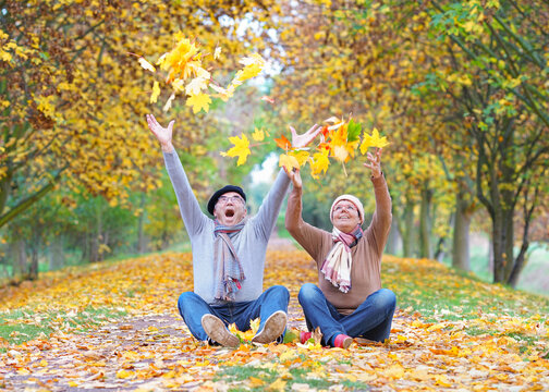 happy senior couple throw up colorful leaves in the autumn forest