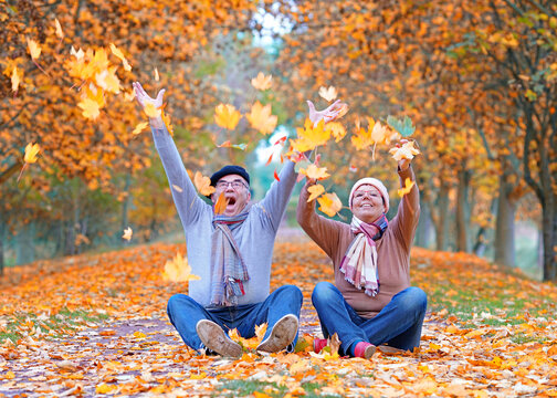 Happy Man and Woman throwing up colorful autumn leaves on a Beautiful Fall Day