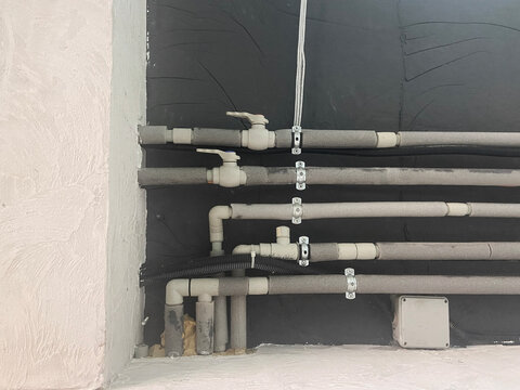 Neatly installed water supply mains, complete with mounts and valves, on a dark wall.