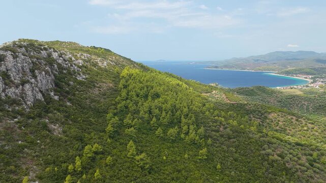 Aerial view of the lush green hills and rocky slopes above the turquoise coastline of Toroni, located in the Halkidiki region of northern Greece