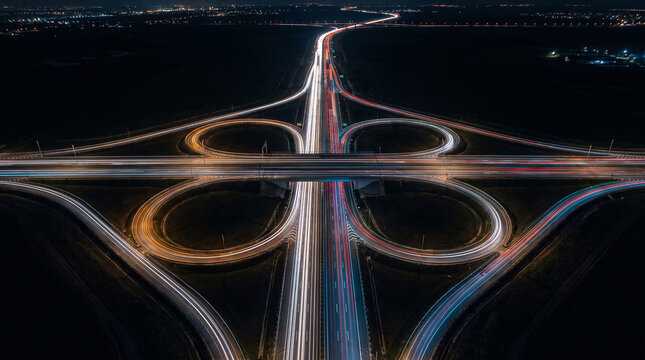 Aerial view of cloverleaf highway interchange with heavy night traffic light trails