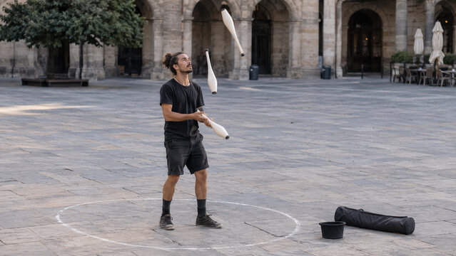 Street performer juggling clubs in a historic city plaza during outdoor performance. Concept of busker, circus artist, juggler, entertainer.