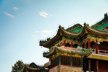 Fototapeta premium Detailed view of a traditional Chinese temple featuring green glazed tile roofs and ornate red wooden architecture under a clear blue sky.