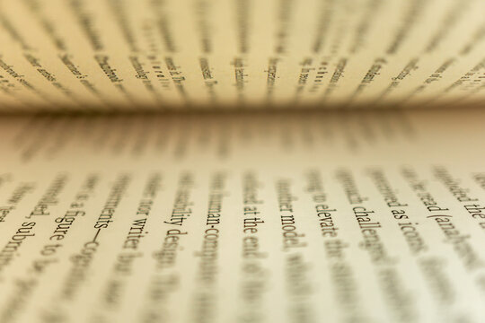 Open book with focused lines of text amid soft blurred foreground and background, highlighting typography and depth of field for study, reading, learning and research imagery