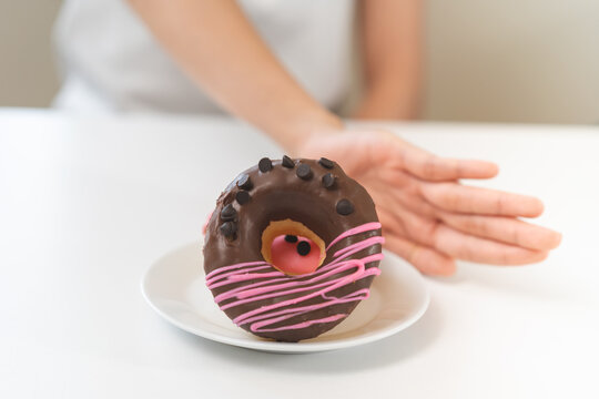 Diet concept, asian young woman hand push out, deny sugar donut, doughnut and sweet taste food on plate, fighting to keep it from getting fat when person bring to me. Healthy nutrition of weight loss.