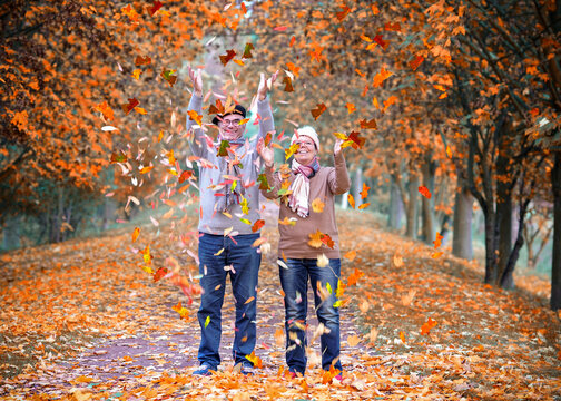 Cheerful Couple throw up Golden Autumn Leaves in Warm Sunlight