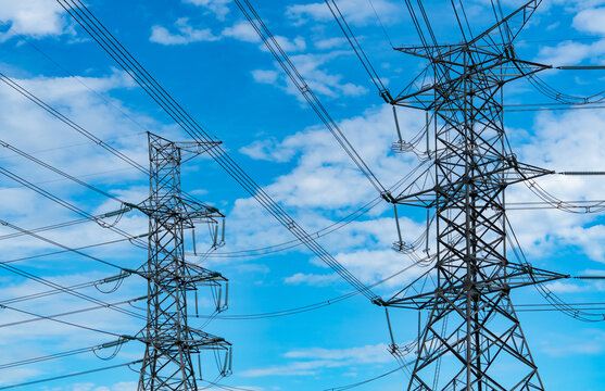 High voltage electricity transmission towers and power lines against blue cloudy sky, large scale electrical grid infrastructure supplying energy for cities, industry and modern development.