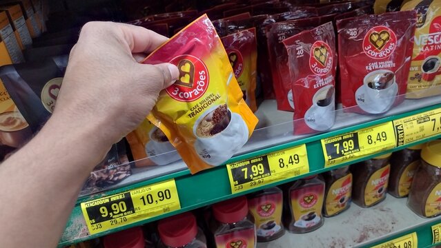 ITABIRA, BRAZIL - SEPT 19, 2026: Hand taking a 40g pouch of 3 Coracoes instant coffee from a supermarket shelf with price tags showing R$ 7.99 and R$ 8.49, highlighting retail inflation and costs.