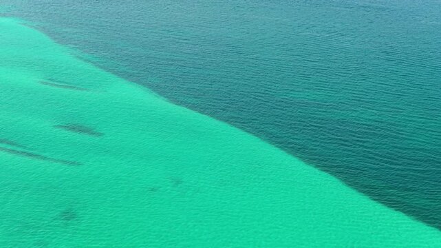 Aerial view of a striking contrast between shallow turquoise and deeper blue waters in the sea off Vourvourou, Halkidiki, Greece