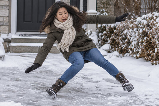 Young Asian woman slipping and falling on an icy driveway covered in snow during winter