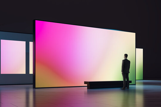 Businessman Viewing a Large Colorful Display Screen in a Modern Exhibition Interior, Blank Mockup for Branding, Presentation, Design, and Creative Concepts.