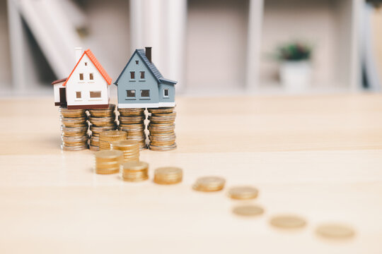 Two miniature houses on coin stacks with a trail of money symbolize property investment growth, real estate wealth, portfolio building, home equity, savings progress, and long-term financial goals.
