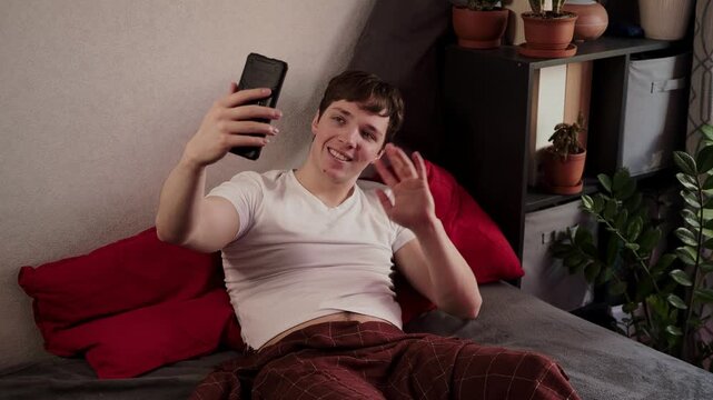 Young handsome guy uses mobile phone before sleep lying in bed and chatting with women to meet and seduce. Attractive man with the help of smartphone meets mistress and flirts