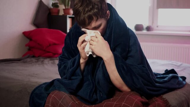 Sick guy with cold, flu or virus illness with cough and running nose lying in bed and using tissues. Sneezing ill guy at home. Man and health