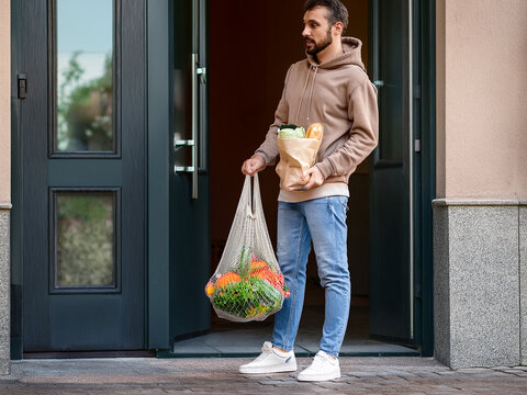 男性が買い物袋とネットで野菜を抱えて家から出てくる