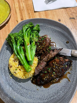 Sliced kangaroo steak with green peppercorn sauce, broccolini and saffron rice on a speckled plate