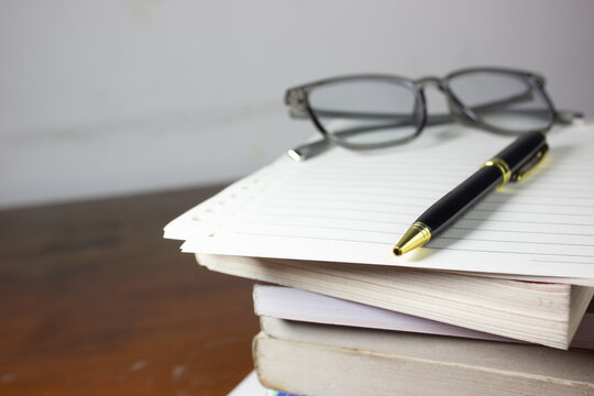 Close-up photo of eyeglasses on a stack of books, symbolizing university study, thesis, academic journals, research, student assignments, study sessions, overtime work, and professional responsibiliti