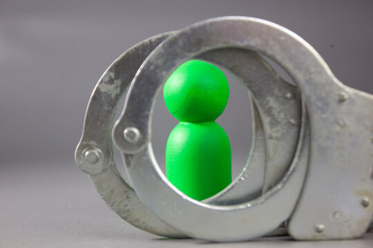 Conceptual photo of a green peg doll wearing handcuffs, symbolizing a scapegoat, wrong suspect, false accusations, unintended involvement, ambiguous cases, wrongful judgment, punished  despite