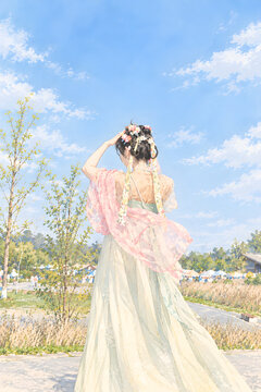 Chinese woman in flowing hanfu viewed from behind beneath a blue spring sky