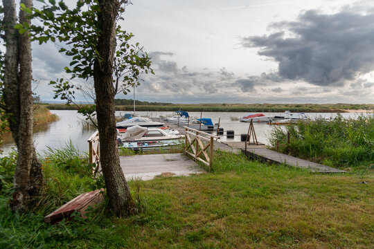 Small motorboats and leisure craft are moored beside wooden docks in a sheltered marina bordered by reeds and trees. Natural waterfront setting for recreational boating, fishing, summer vacation, mari