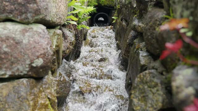 Water flows from pipe down rock canal with green and red leaves