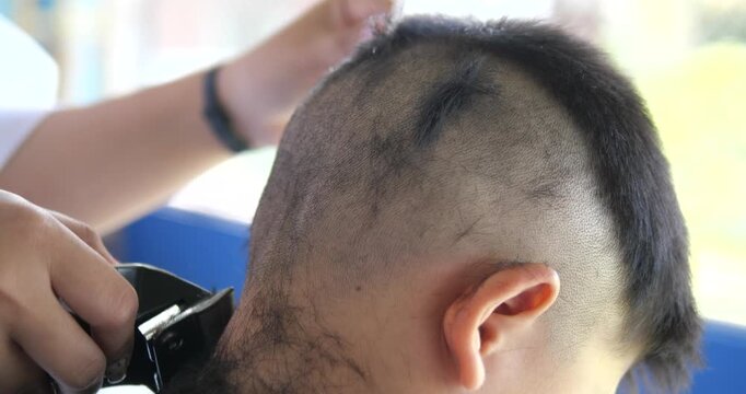 Close up of barber using electric hair clipper to cut man short hair in barbershop
