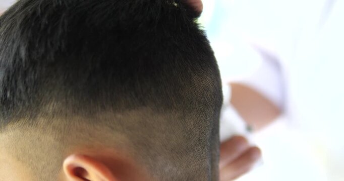 Close up of barber using electric hair clipper to cut man short hair in barbershop