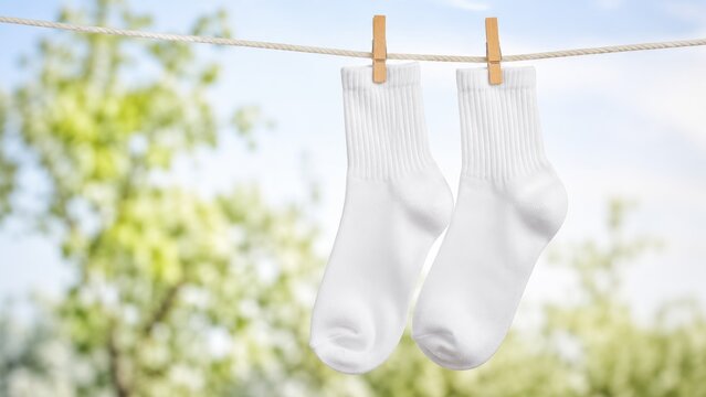 Pair of white ankle socks hanging on a clothesline outdoors, clipped with wooden clothespins against a blurred green background
