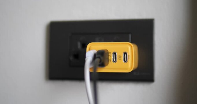 Close up of yellow multi-port fast charger plugged into wall outlet with USB cables