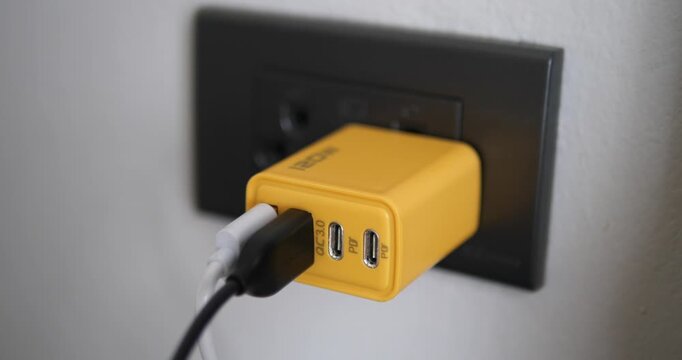 Close up of yellow multi-port fast charger plugged into wall outlet with USB cables