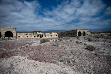 ABADES, TENERIFE, SPAIN - APRIL 24, 2025: Wide side view of the abandoned Sanatorio de Abona complex beneath dramatic clouds. © Peter