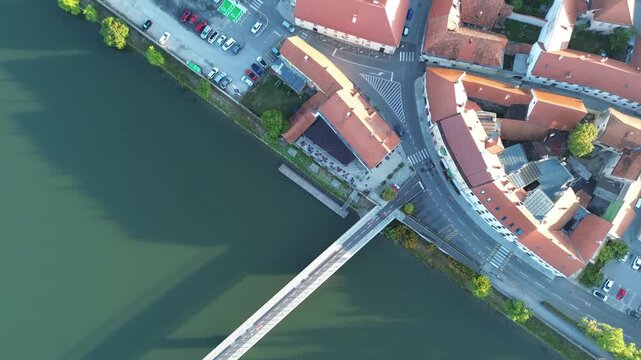 Aerial view of historic Ptuj in Slovenia, showing red tiled rooftops, the Drava River, pedestrian bridge, riverside streets and the charming old town.