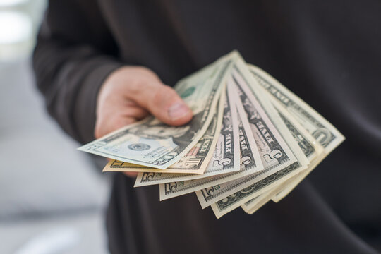 A man in a dark sweatshirt is holding US dollars in his hand.
